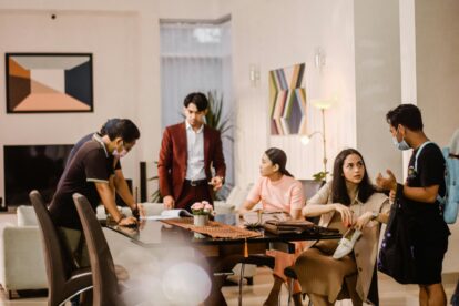 Group of coworkers in a bright lounge discussing documents around a glass conference table, mid-meeting.