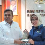 Man in a white shirt and a woman in a hijab pose with a halal indonesia trophy in an office setting