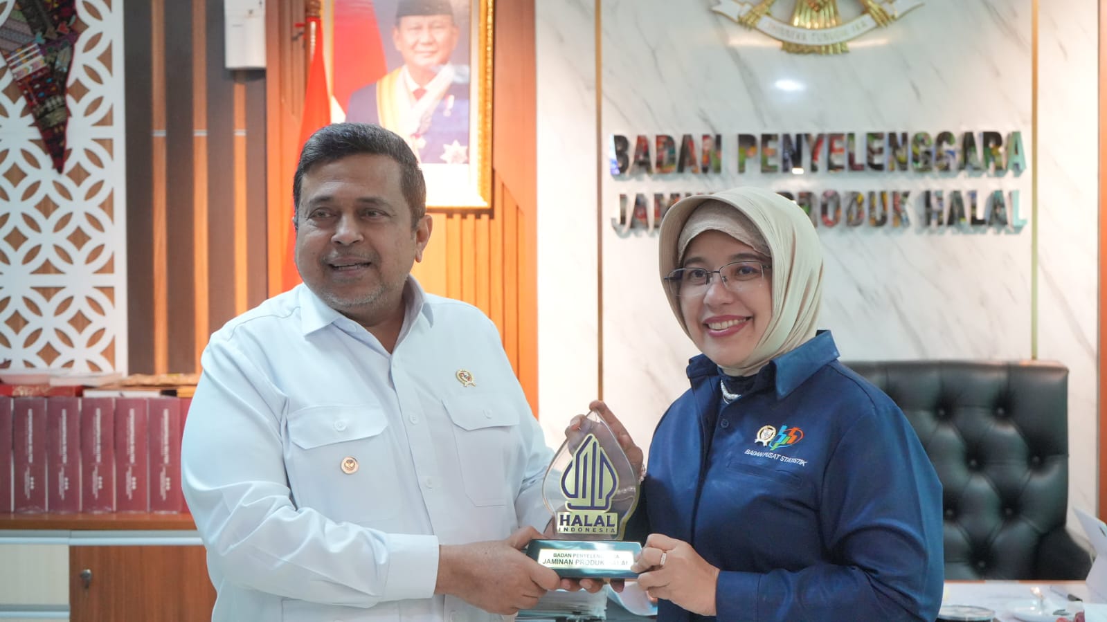 Man in a white shirt and a woman in a hijab pose with a halal indonesia trophy in an office setting