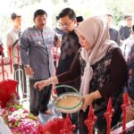 Group of people mainly women in hijabs placing flowers and petals at a shrine behind a red fence while others observe