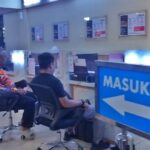 Waiting area at a service counter in a public office two people sit facing desks with a blue masuk sign and a left arrow nearby