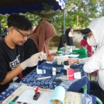 Outdoor medical screening station with a nurse in ppe and volunteers testing at a table under a canopy