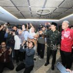 Group of reporters and photographers surrounding two men taking photos in a hallway lobby setting