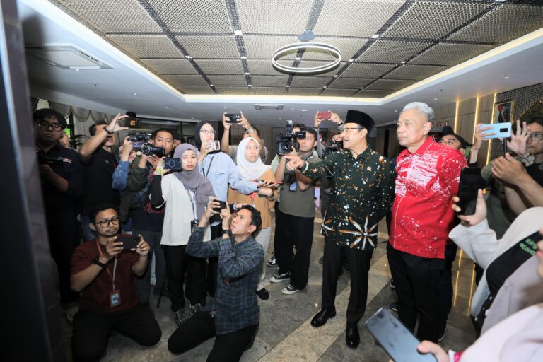 Group of reporters and photographers surrounding two men, taking photos in a hallway lobby setting.