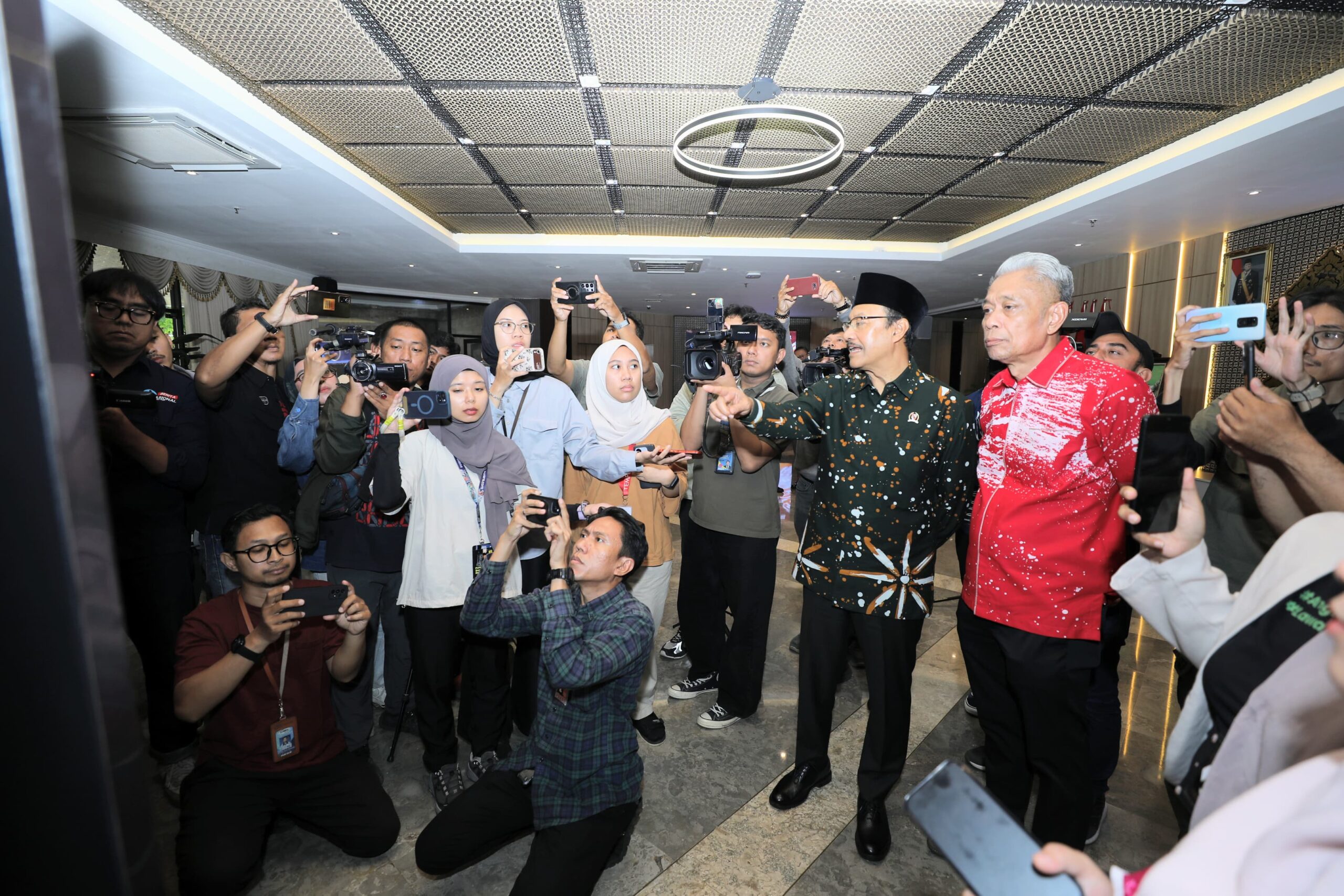 05sos catrawarta Group of reporters and photographers surrounding two men taking photos in a hallway lobby setting