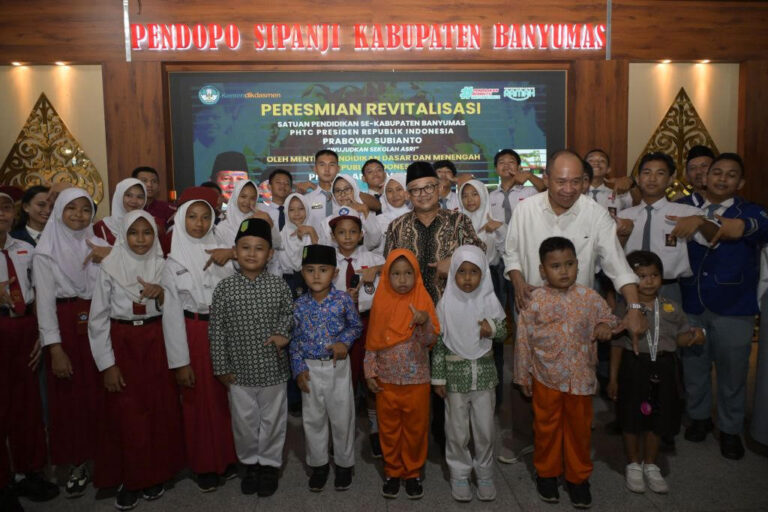 Group of students in uniforms and traditional outfits posing with officials at a ceremony titled 'Peresmian Revitalisasi'.