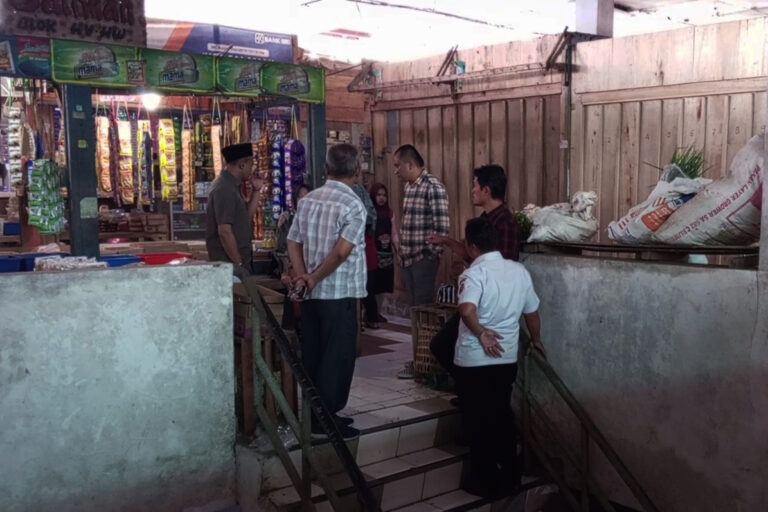Group of men standing on a stairwell in a busy market, conversing near a shop with hanging dried snacks in view.