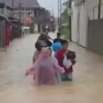 People wading through knee deep floodwater on a residential street