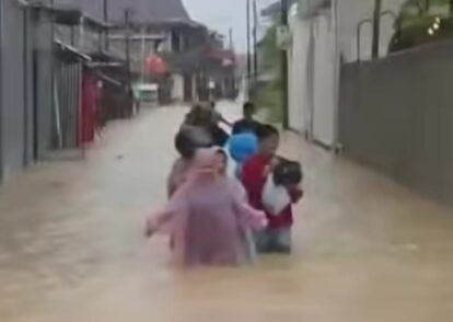People wading through knee-deep floodwater on a residential street.
