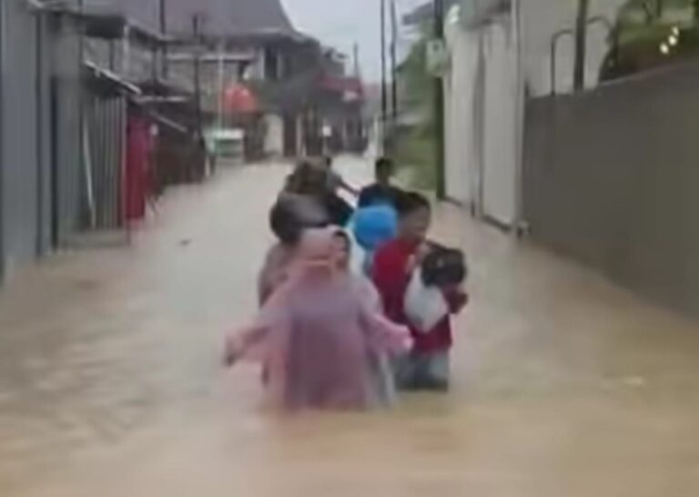 People wading through knee-deep floodwater on a residential street.