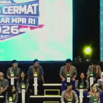 Contestants seated on a tiered stage wearing matching patterned shirts and green id badges during a competition window of a quizcontest event