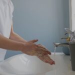 Person washing hands with soap at a bathroom sink water running from the faucet nearby