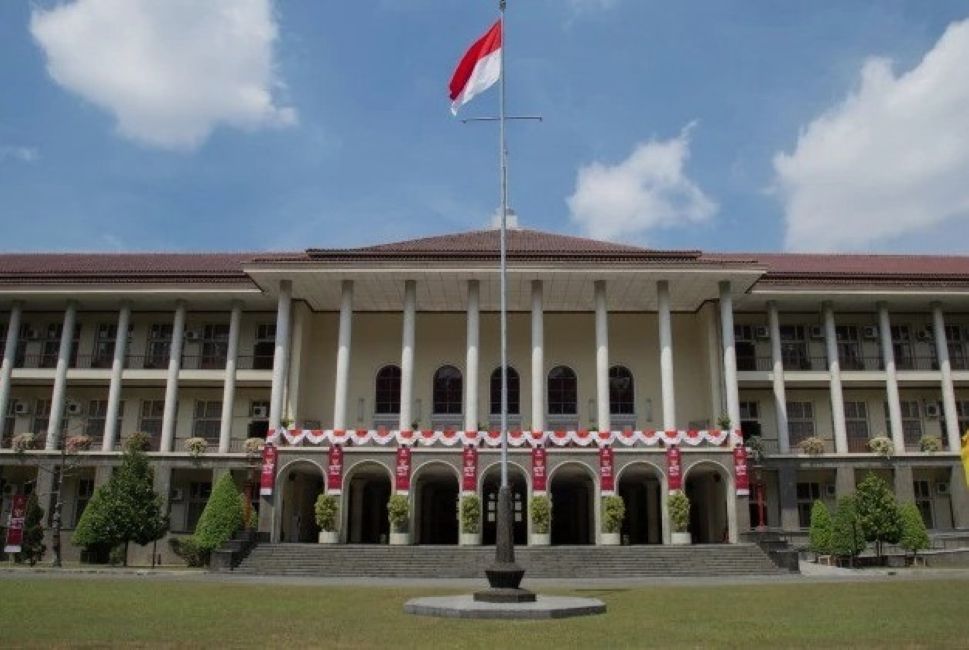 Front view of a neoclassical campus building with tall columns arches and a central flagpole flying a red and white flag with decorative banners along the facade