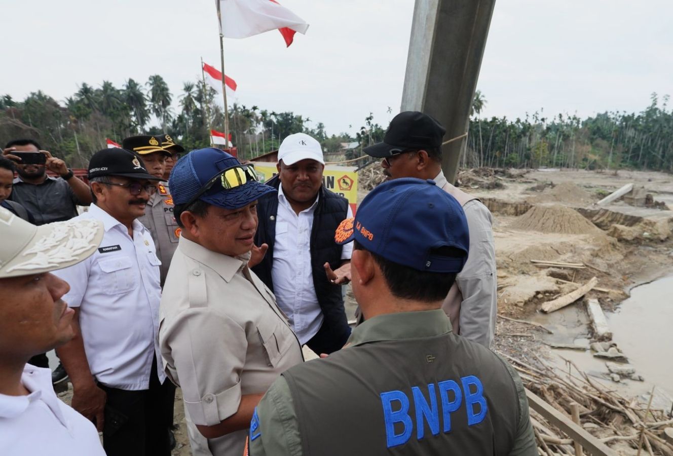 Group of indonesian officials in uniform and caps inspecting a constructionsite with sand piles and a damaged riverbank flags in the background