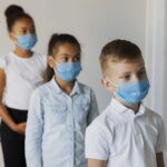 Three children in a hallway wearing blue face masks lined up in a row