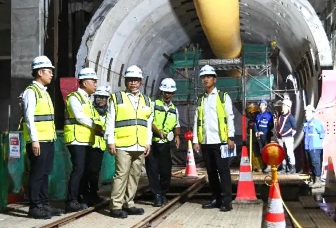14ewapres catrawarta Group of construction workers in hard hats and high visibility vests standing inside a tunnel with a large yellow boring machine part overhead posing for a photo inside a work zone