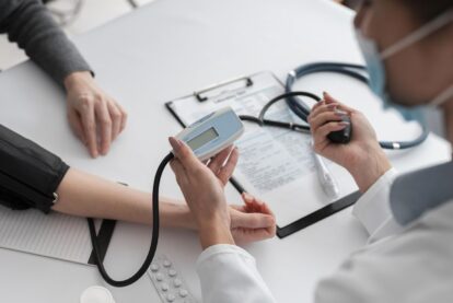 Healthcare professional checks a patient’s blood pressure using a digital cuff and monitor on a clinic table.