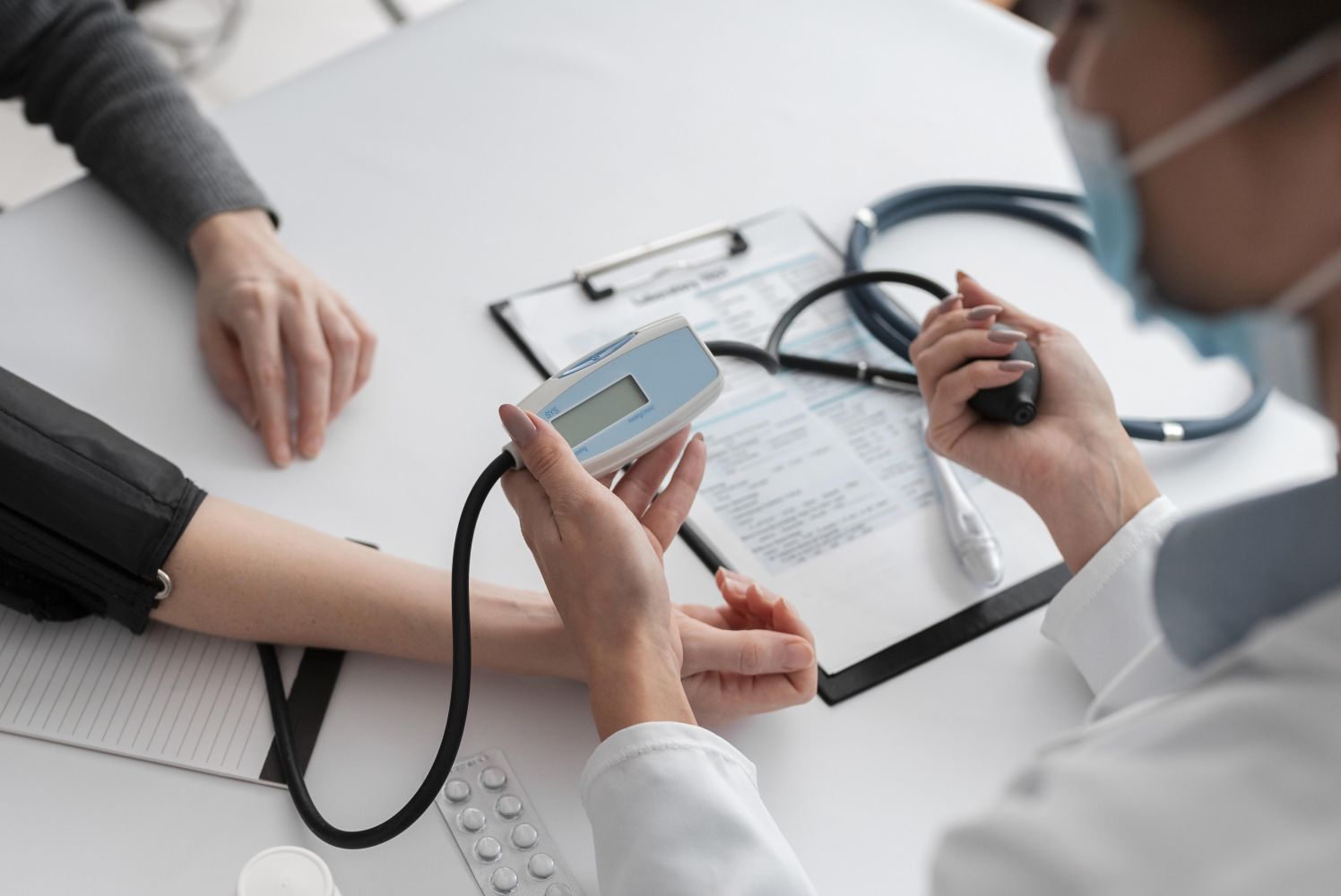Healthcare professional checks a patients blood pressure using a digital cuff and monitor on a clinic table