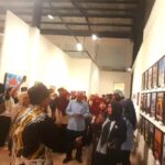 Crowd of people in a white walled art gallery viewing framed posters on the wall