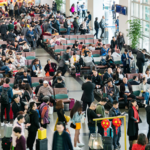 Busy airport terminal filled with travelers waiting and moving through seating area with luggage