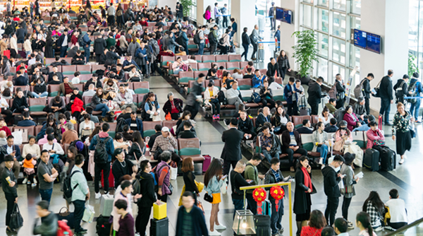 Busy airport terminal filled with travelers waiting and moving through seating area with luggage