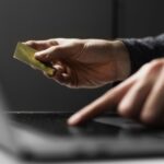 Person holding a gold credit card above a laptop keyboard suggesting an online payment