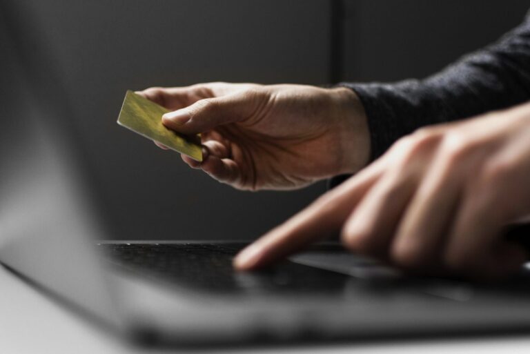 Person holding a gold credit card above a laptop keyboard, suggesting an online payment.
