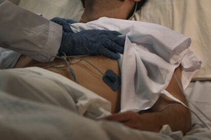 Medical professional wearing blue gloves resting a hand on a patients back in a hospital bed