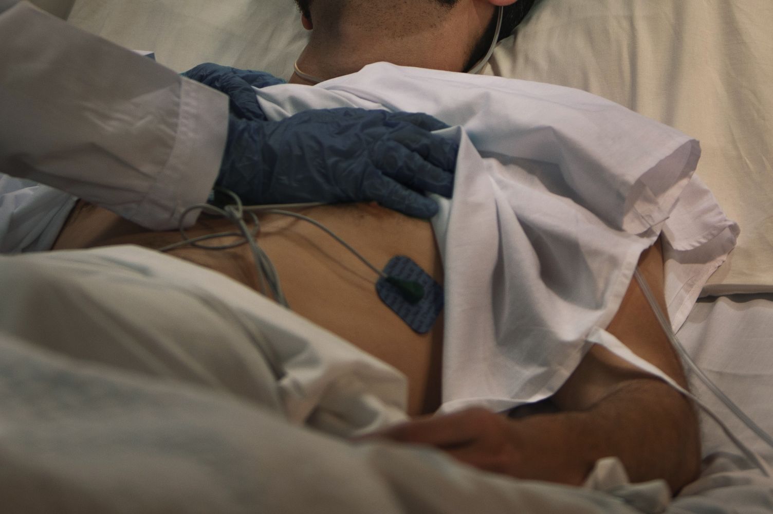 Medical professional wearing blue gloves resting a hand on a patients back in a hospital bed