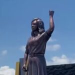 Bronze statue of a man with his right fist raised outdoors against a blue sky with clouds