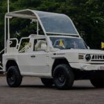 White vintage off road suv with a clear curved canopy parked in an open square during an event