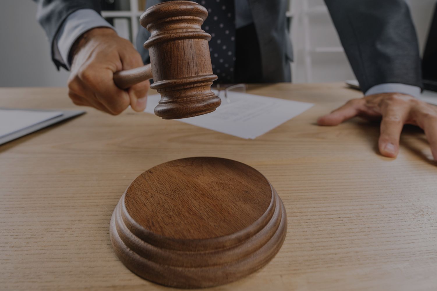 17ehakim catrawarta Judges gavel about to strike a wooden sound block on a desk with a hand resting nearby and papers in the background