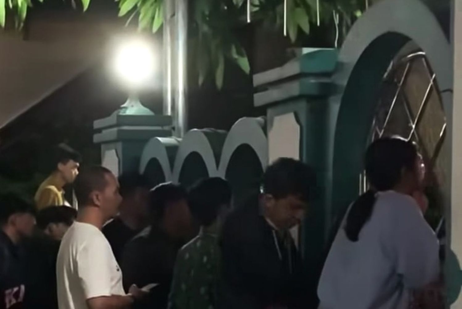 18enobar catrawarta A crowd of people standing in line outside a decorative green building with rounded arches at night illuminated by a bright streetlamp
