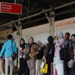 People line up at a train station platform in yogyakarta waiting with luggage under a no smoking sign