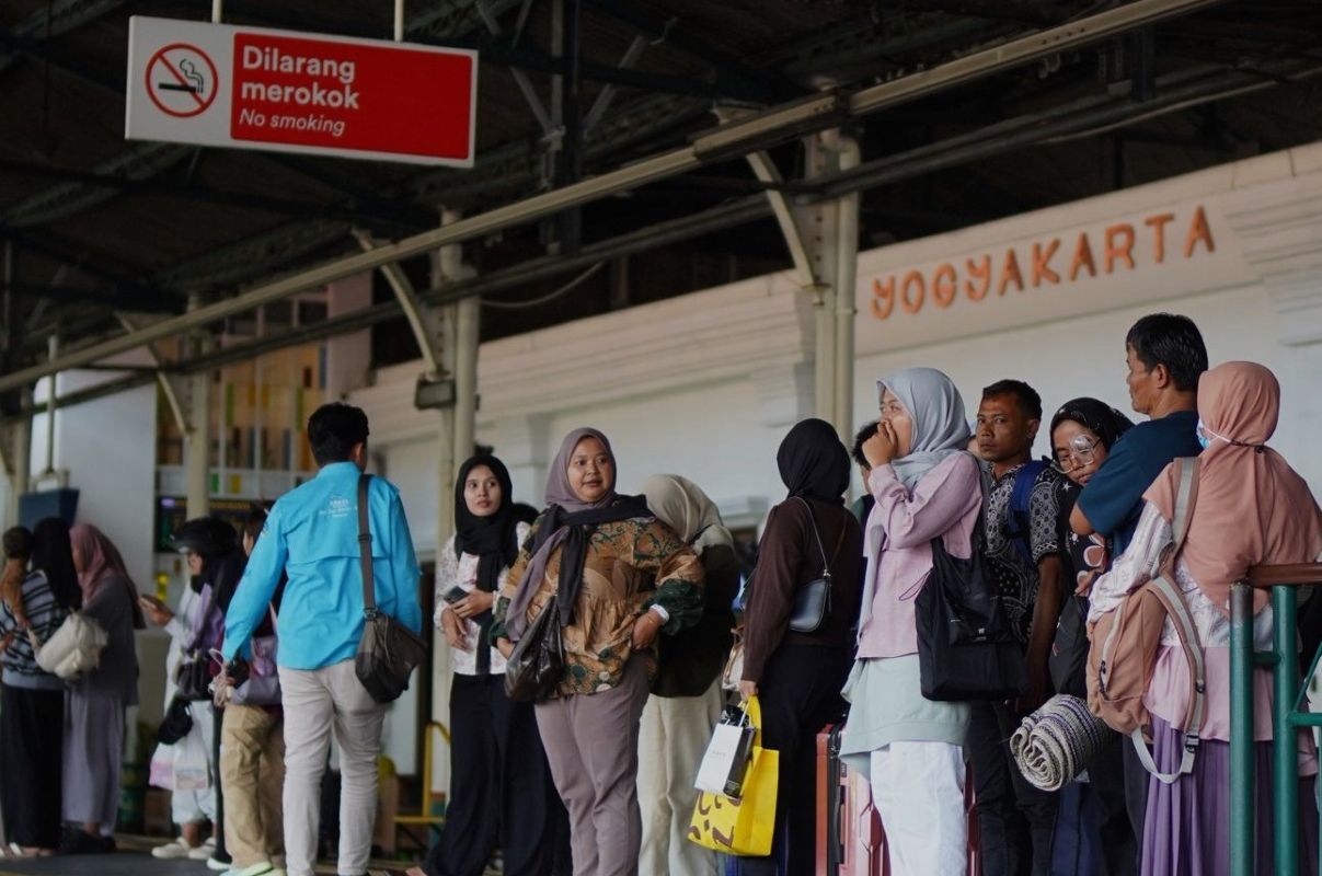 People line up at a train station platform in yogyakarta waiting with luggage under a no smoking sign
