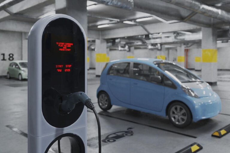Blue electric car plugged into a charging station in a dim parking garage with another car in the background.