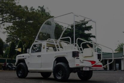 White open-top safari tour vehicle with elevated seating and glass canopy, parked outdoors.