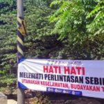 Officer standing beside a safety banner that reads hati hati melewati perlintasan sebidang utamakan keselamatan budayakan tertib