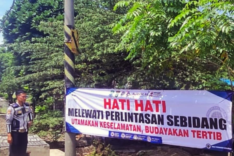 Officer standing beside a safety banner that reads hati hati melewati perlintasan sebidang utamakan keselamatan budayakan tertib