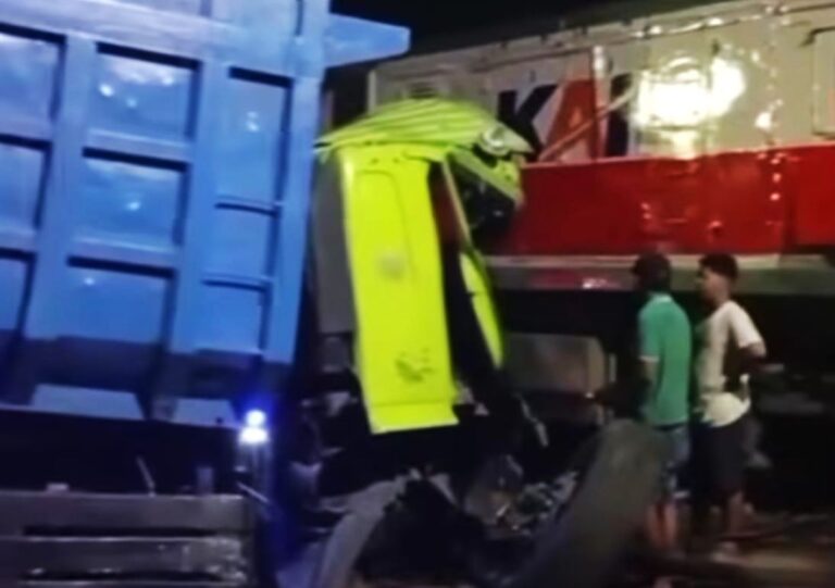 Nighttime accident scene with a blue container truck and a bright yellow safety-vested worker inspecting the cab area, two bystanders nearby.