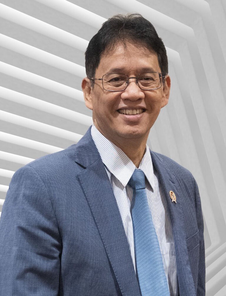 Portrait of a smiling man in a blue suit, striped shirt, and light blue tie, wearing glasses.