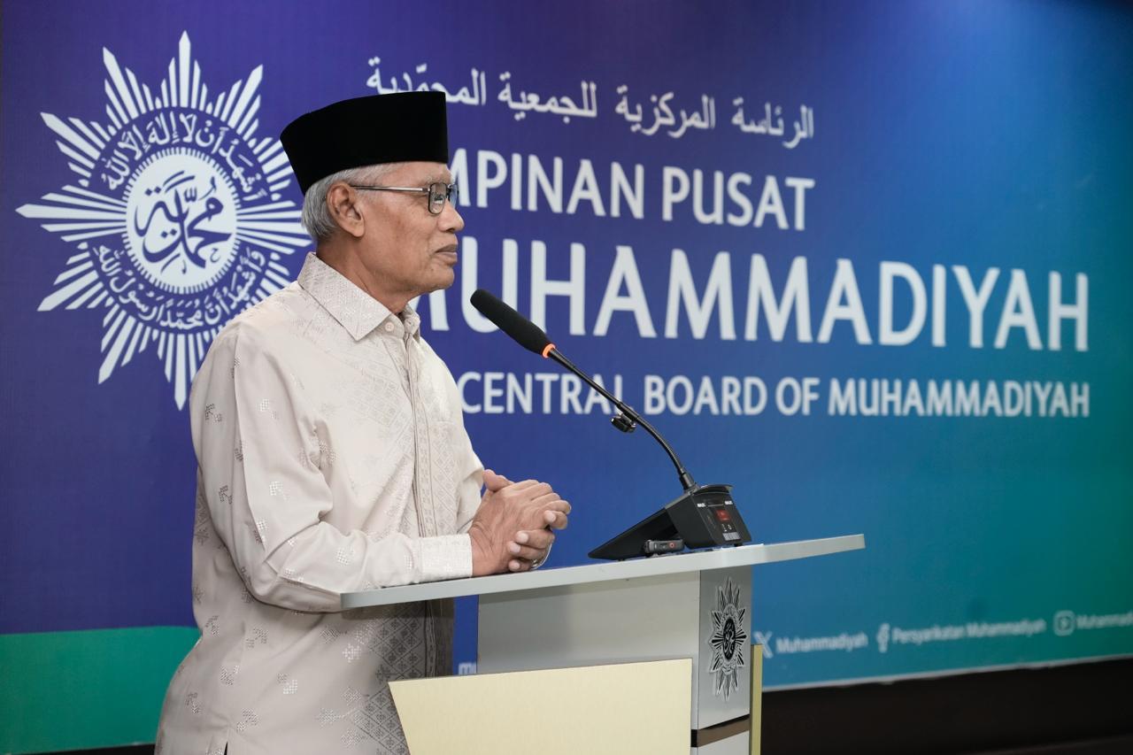 Man in a white embroidered kurta and black cap speaks at a podium with a blue backdrop reading central board of muhammadiah