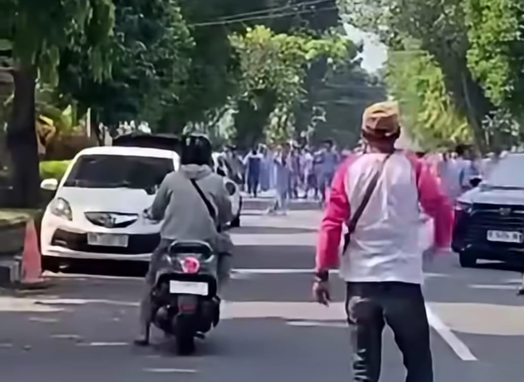 Group of people marching down a tree lined street as vehicles pass seen from behind the rider and oncoming traffic