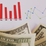 Red bar chart and bluegreen line chart above overlapping dollar bills depicting financial data trends