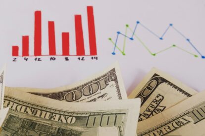 Red bar chart and blue/green line chart above overlapping dollar bills, depicting financial data trends.