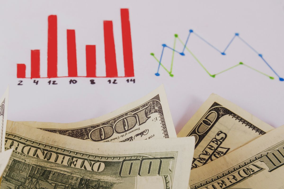 Red bar chart and bluegreen line chart above overlapping dollar bills depicting financial data trends