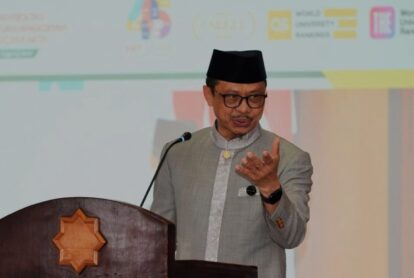 Man wearing a black peci and gray suit giving a speech at a wooden podium with a star shaped emblem microphone nearby