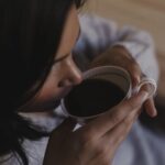 Close up of a person sipping from a white mug hands holding the mug near a dark coated face in a soft warm setting