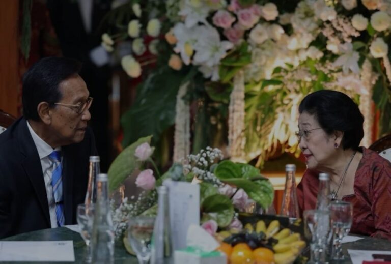 Two older adults in formal attire converse at a table decorated with flowers and fruit, with bottles and glasses nearby.