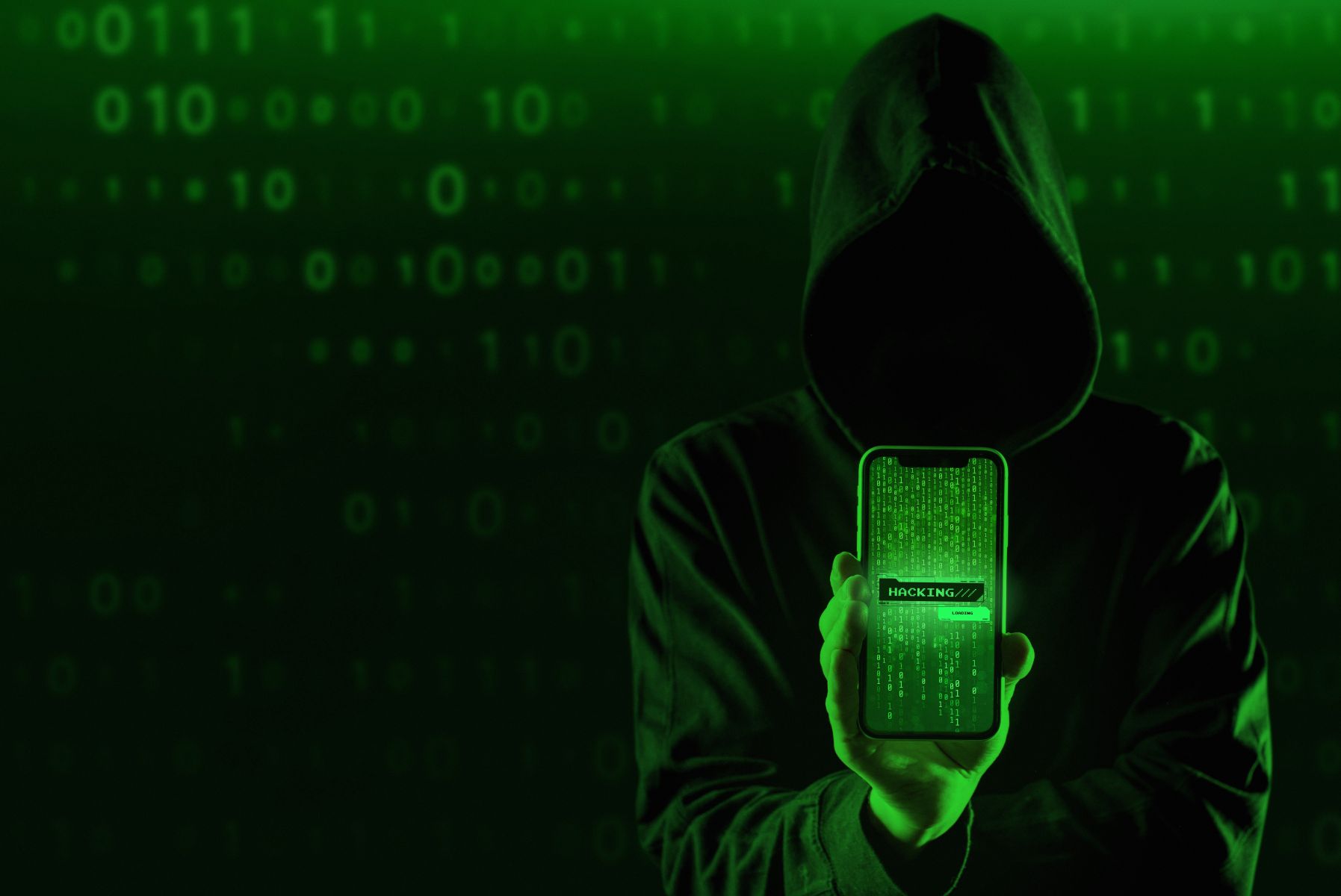 25etipu catrawarta Hooded figure in dark hoodie displays a phone with a glowing hacking screen against a green digital background of binary code